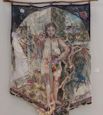 Tapestry created from fabric pieces, showing a female figure interacting with her home setting, which includes a blue ladder-back chair, a curtained window, a hardwood floor, a carpeted floor and a wall with floral wallpaper.