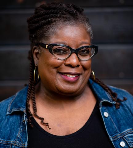 Headshot of Sheryl Wilson in blue and black against a brick-wall background