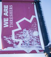 A "WE ARE THRESHERS" sidewalk banner with snow on the corner